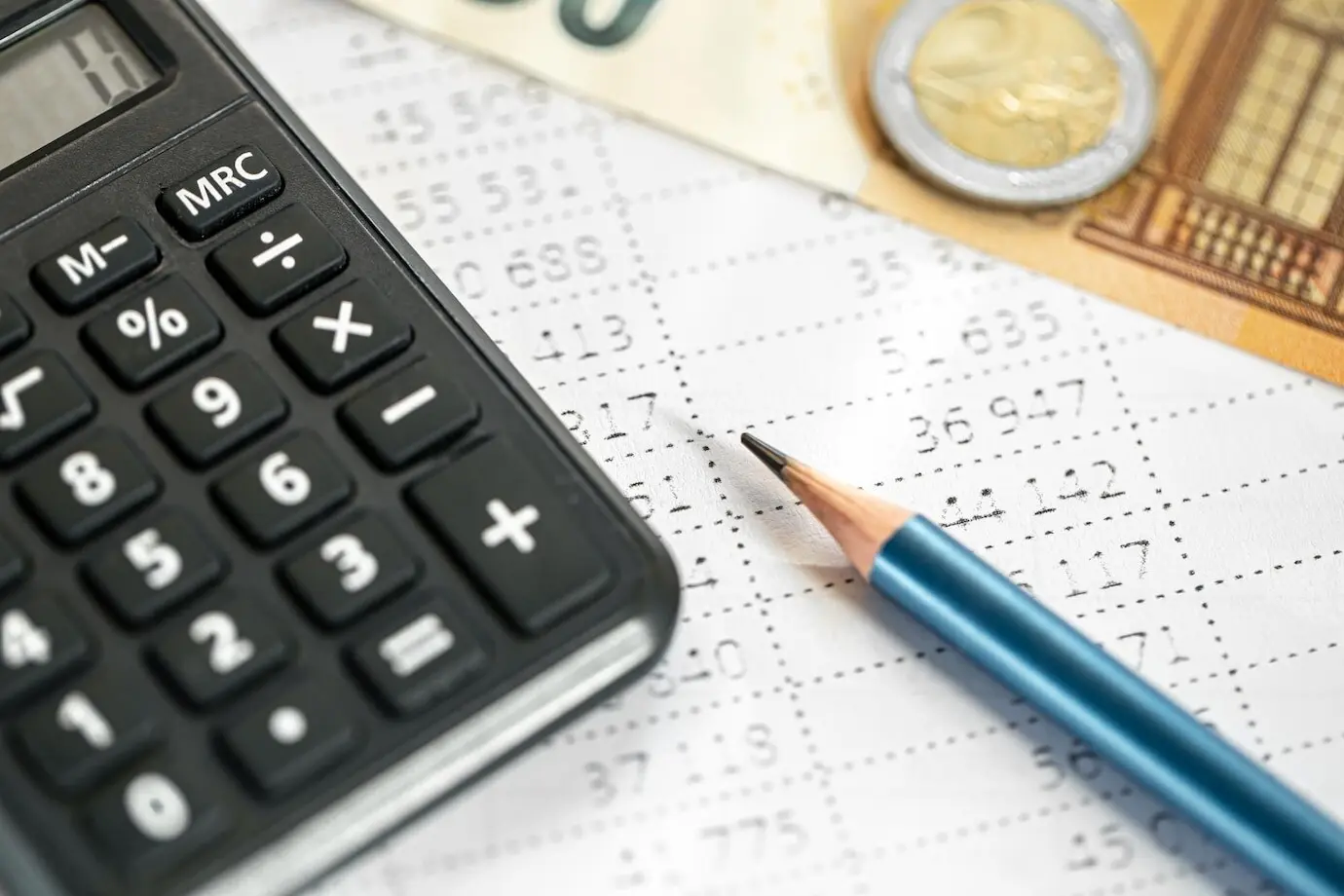 Close-up of a calculator, money, and a pencil against a blurred background.