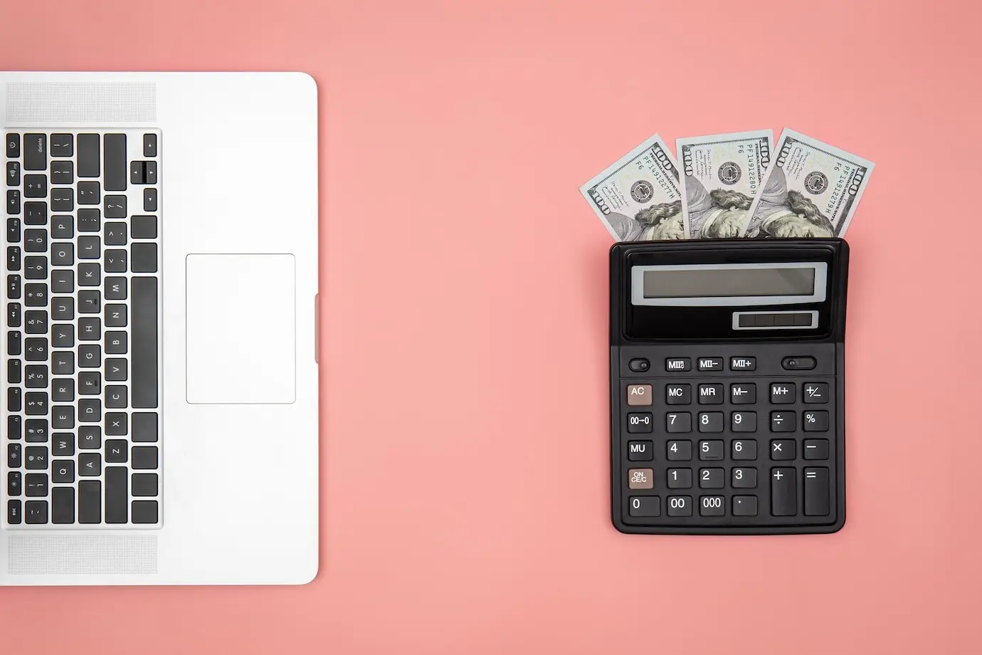 Flat lay of a calculator, laptop, and dollar bills on a colored background.